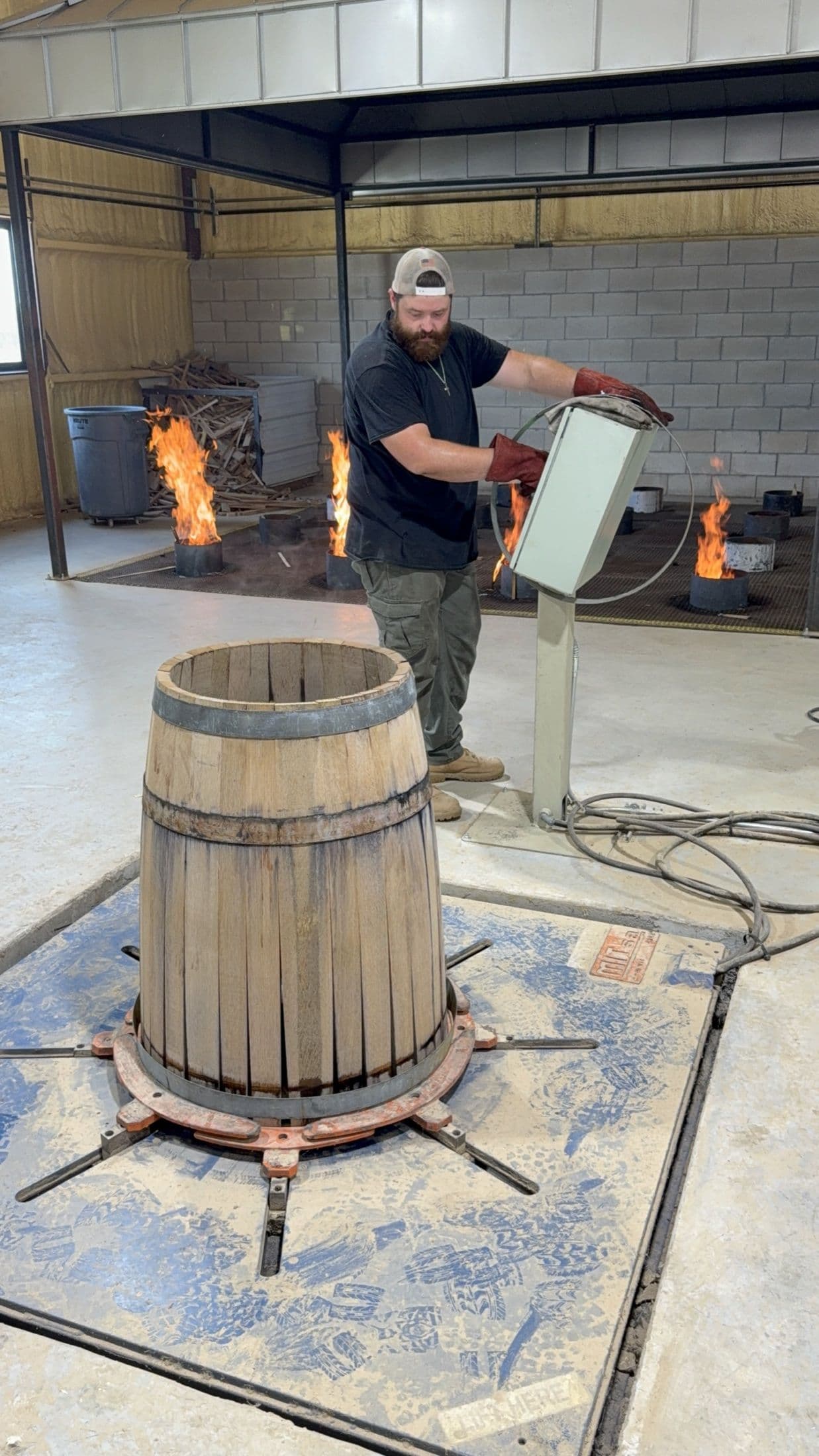 Cooper wearing heat-resistant gloves beside a raised barrel on the Standard Cooperage firing floor